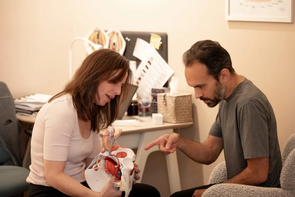 Therapist using a pelvic anatomy model to explain treatment to a male patient