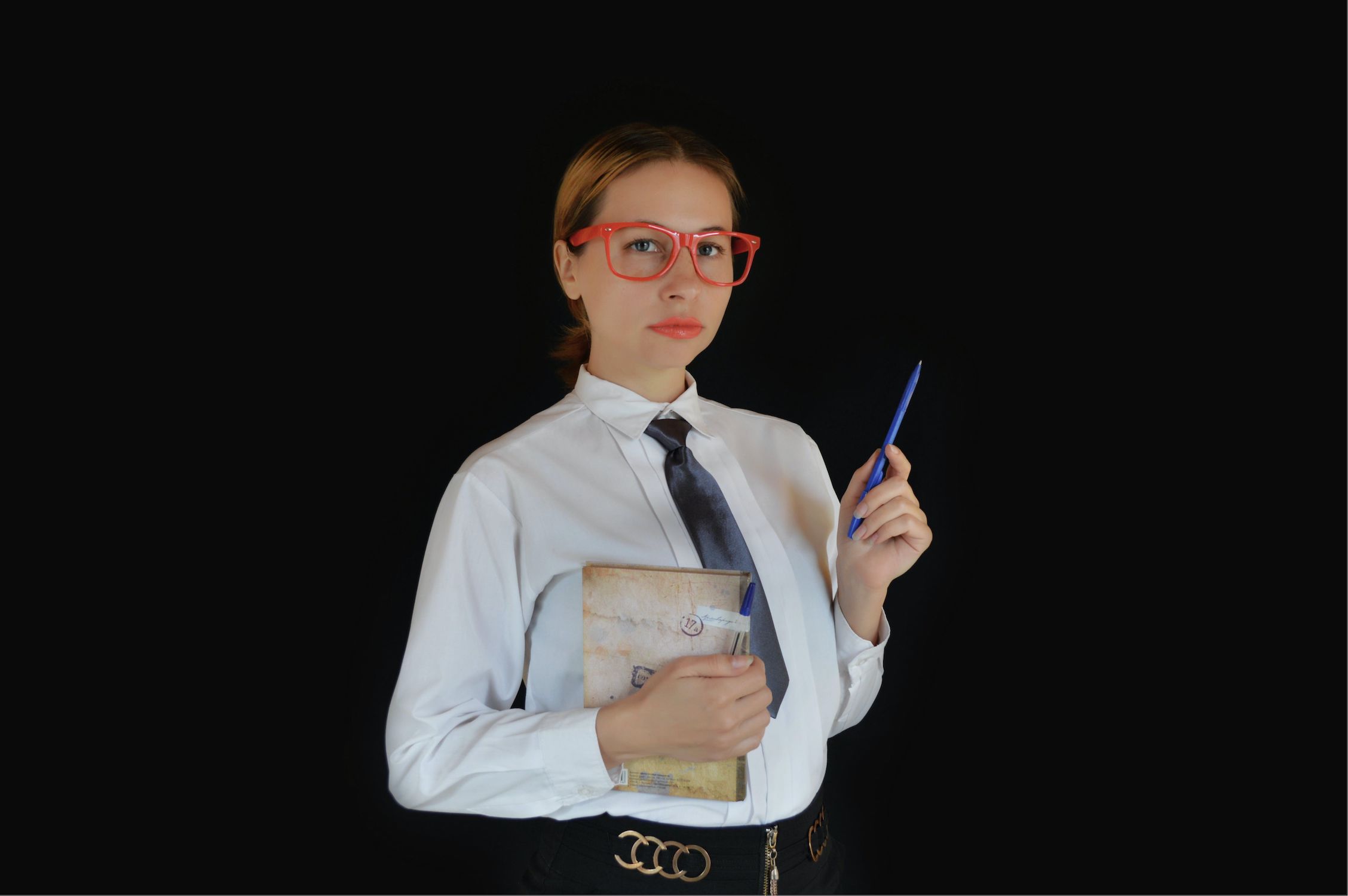 An image of a therapist in professional clothes: a button up shirt and tie. She is holding a pen and notepad and has a serious expression.